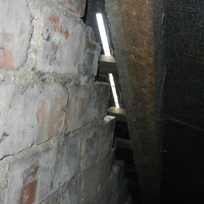 Slipped slates clearly visible from within this roof void. This is often caused by some slight settlement of the roof structure leading to the slates bridging on the party dividing walls in the loft forcing them loose. Nail sickness also often accompanies this problem where widespread corrosion of the nails holding the slates occurs due to age and slates will slip annually. In this scenario removal and reinstatement of the slate roof covering is advised.&nbsp;
